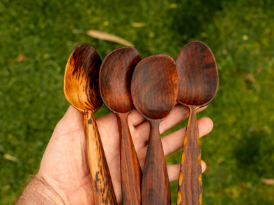 A hand holding four spoons that have been carved from wood