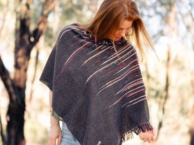 A woman wearing a woven scarf standing in a field looking away from the camera